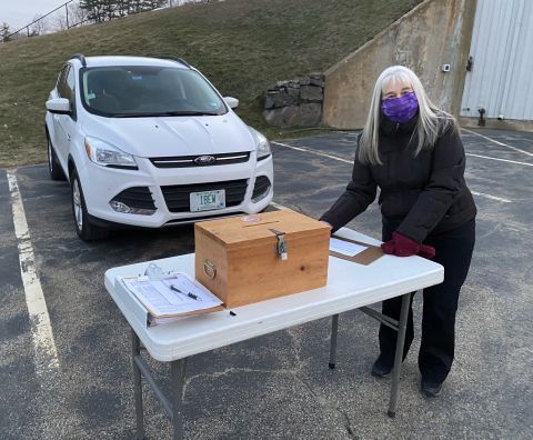 woman at folding table beside ballot box and parked SUV by IBEW 1837