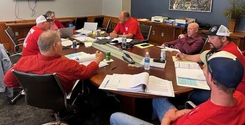 Men in red shirts seated around a conference table in a meeting room by IBEW 1837