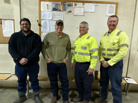 Four men posing indoors in work clothing by IBEW 1837