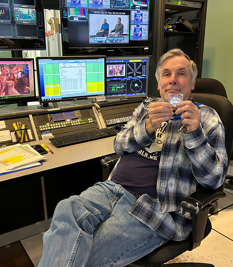 Man seated at control desk holding a medal in a broadcast room by IBEW 1837