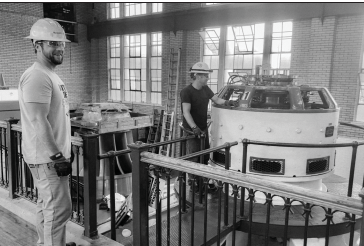 Two workers beside a large industrial machine inside a brick building by IBEW 1837