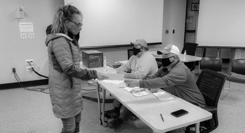 Woman presenting a paper to two masked volunteers at a table by IBEW 1837