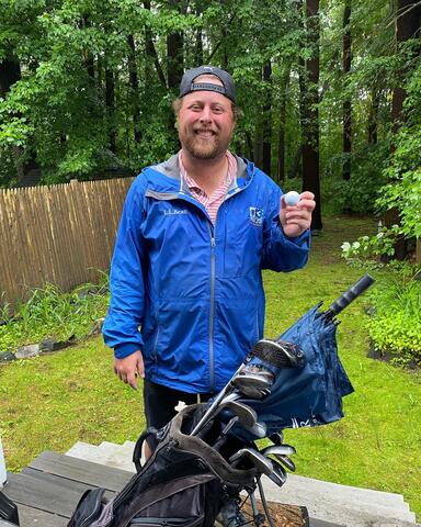Smiling golfer holding a golf ball beside a golf bag by IBEW 1837